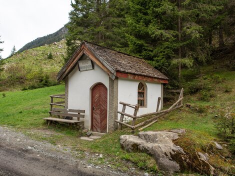 Eine kleine, malerische Hütte steht inmitten einer grünen Landschaft. Umgeben von Bäumen und Bergen bietet sie eine ruhige Atmosphäre. | © Bernhard Gruber – Photography