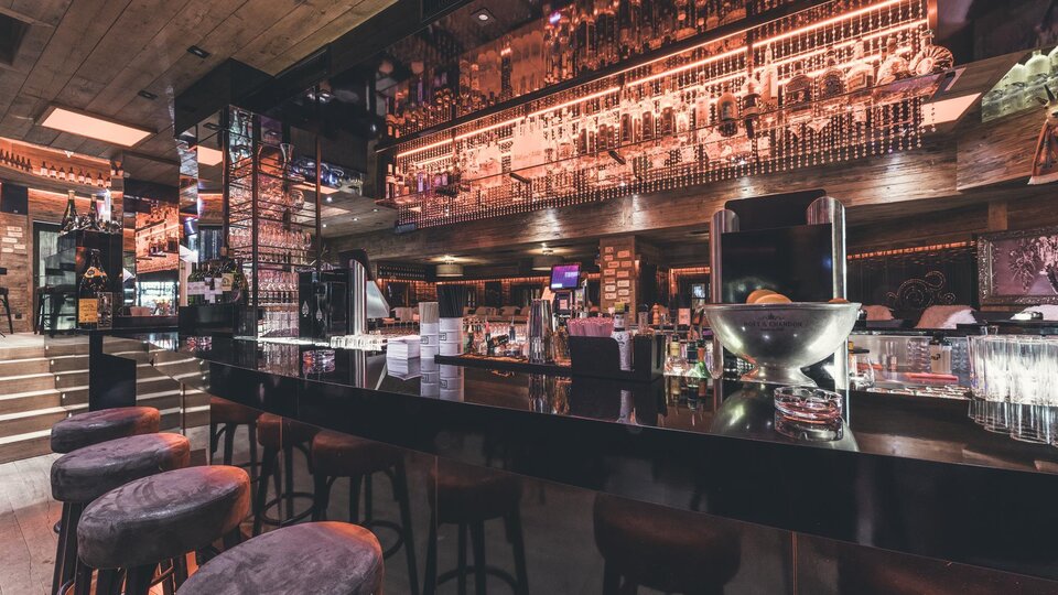 A modern bar with an elegant counter and stylish bar stools. The lighting and decoration create an inviting atmosphere.