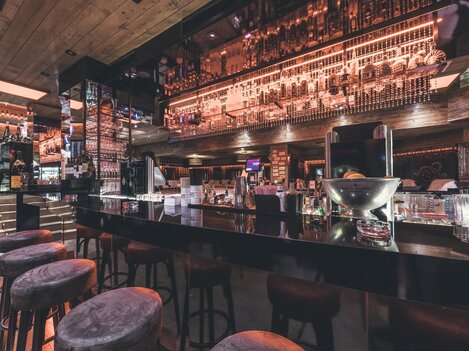 A modern bar with an elegant counter and stylish bar stools. The lighting and decoration create an inviting atmosphere.