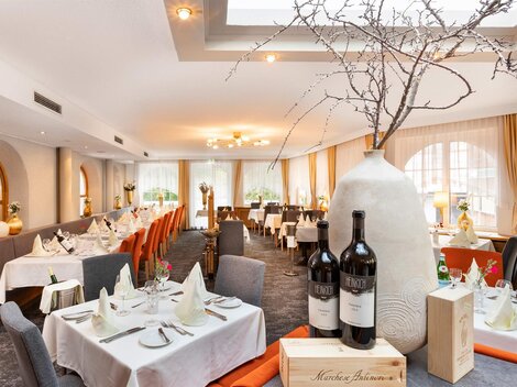Ein elegantes Restaurant mit gedeckten Tischen und stilvoller Dekoration. Ein großer, dekorativer Krug steht im Vordergrund neben zwei Flaschen Wein.