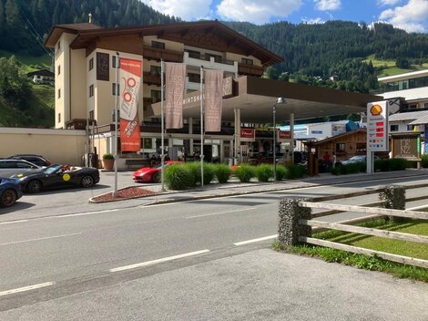 Ein modernes Gebäude mit einem Empfangsbereich und einer Tankstelle im Vordergrund. Umgeben von grünen Hügeln und einer klaren blauen Himmel.