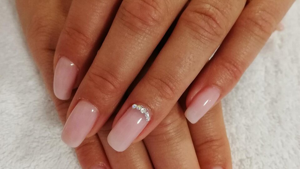 Two hands with freshly manicured, pink nails are resting on a white towel. Some of the nails have small jewels on them.