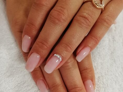 Two hands with freshly manicured, pink nails are resting on a white towel. Some of the nails have small jewels on them.