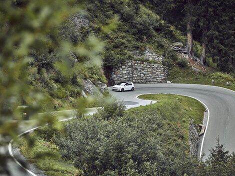 Eine kurvenreiche Straße durch eine grüne Landschaft. Ein Auto fährt um eine scharfe Kurve.