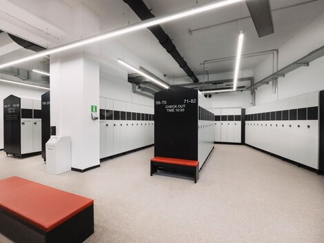 Ein moderner Umkleideraum mit mehreren Spinden in Schwarz und Weiß. In der Mitte steht eine Bank in Orange.