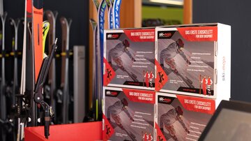 A presentation of ski equipment in a store. Boxes with advertising for products are on a red table.