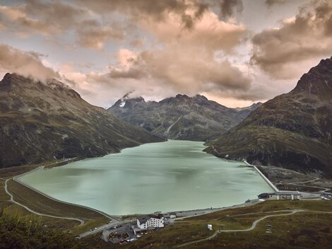 Ein schöner Bergsee, umgeben von hohen Bergen und dramatischen Wolken. Die ruhige Wasseroberfläche spiegelt die umliegende Landschaft wider.