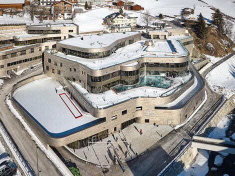 Ein modernes Gebäude in einer schneebedeckten Landschaft mit einem ganzjährig zugänglichen Eisfeld. Die Architektur ist elegant, umgeben von malerischen Bergen und Ferienhäusern.