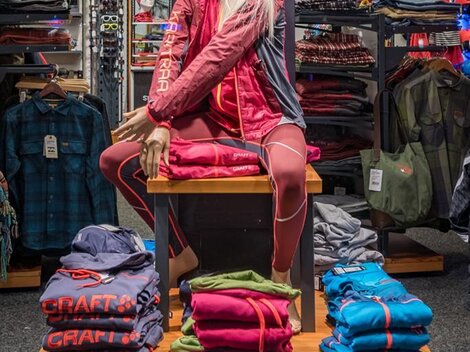 Ein Schaufenster mit einer Puppe, die Sportkleidung von Craft präsentiert. Im Hintergrund sind weitere Kleidungstücke und Accessoires angeordnet.