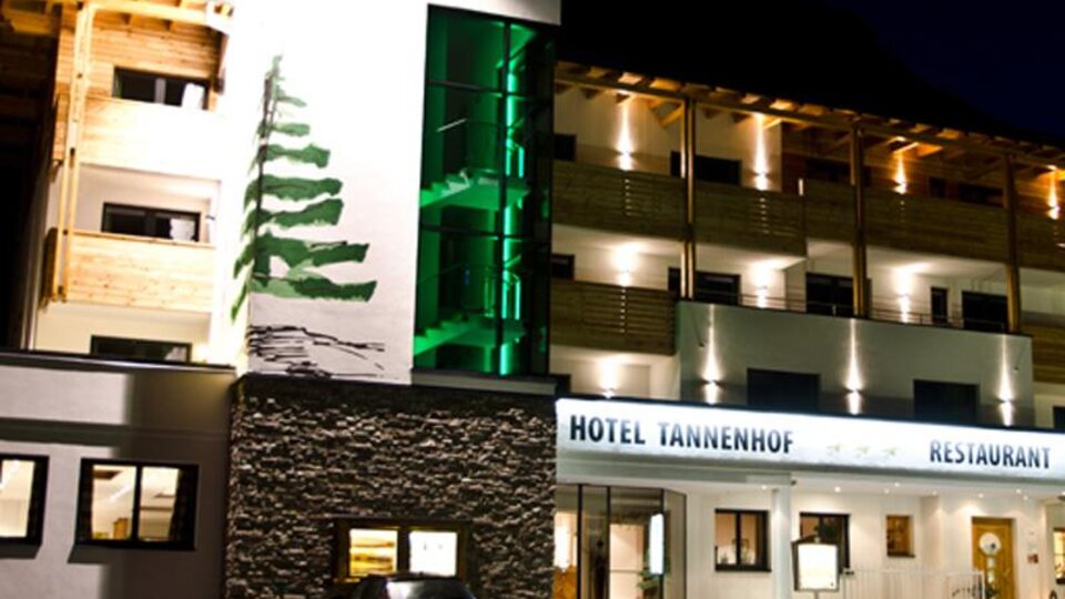 A modern hotel with a wooden facade and pleasant lighting at night. The Hotel Tannenhof offers an inviting atmosphere and a dining area.