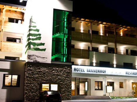 A modern hotel with a wooden facade and pleasant lighting at night. The Hotel Tannenhof offers an inviting atmosphere and a dining area.