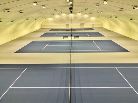 Eine moderne Tennishalle mit mehreren Spielfeldern. Die blauen Plätze sind gut beleuchtet und bieten Platz für mehrere Spiele.