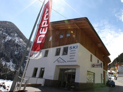 Ein modernes Geschäft mit Holzfassade, das Ski-Verleih und -Verkauf anbietet. Die Umgebung ist bergig und schneebedeckt.