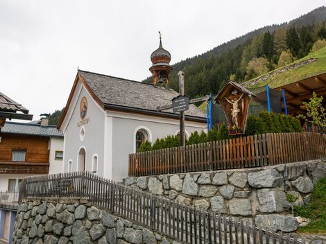 Eine kleine Kirche mit einer markanten Kuppel und einem hübschen Garten. Im Hintergrund sind grüne Berge zu sehen. | © Bernhard Gruber – Photography