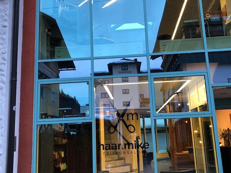 Ein modernes Friseurstudio mit großen Glasfenstern. Der Name "naar.mike" ist prominent an der Tür sichtbar.