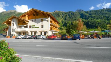 A beautiful hotel with Alpine views and typical wooden architecture. In the foreground, various cars are parked along the street.