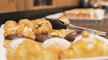 A selection of delicious baked goods, including croissants and chocolate doughnuts. In the background, more treats can be seen.