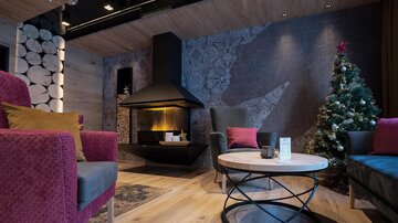 A cozy room with a modern fireplace and a Christmas-decorated fir tree. The furniture in warm colors creates an inviting atmosphere.