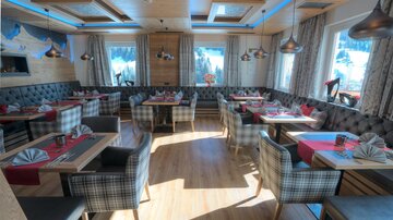 A cozy restaurant with wooden furniture and beautifully decorated tables. Large windows offer a view of the landscape.