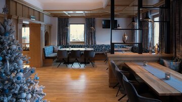 A modern restaurant with bright wooden furniture and a festively decorated Christmas tree. The atmosphere is cozy and inviting.
