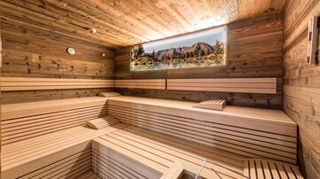 A modern sauna made of light wood with multiple rows of benches. A picture of a mountain landscape decorates the wall and creates a relaxing atmosphere.