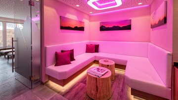 A modern relaxation area with comfortable seating and gentle pink lighting. Wall paintings in soft colors complement the cozy atmosphere.