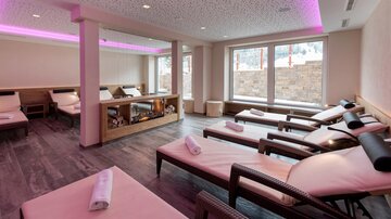 A cozy wellness area with loungers and soft lighting. Large windows offer a view of nature.