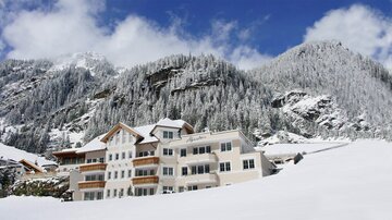 A beautiful hotel in a snowy landscape. In the background, tall, forested mountains rise under a clear sky.