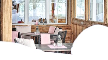 A cozy restaurant with wooden paneling and large windows. The tables are elegantly decorated in bright colors.