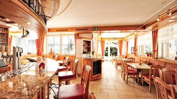 An inviting restaurant with wooden furniture and a bright, friendly atmosphere. The large windows offer a view of nature.
