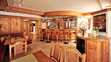A cozy bar with wooden paneling and modern chairs. The space conveys an inviting atmosphere.