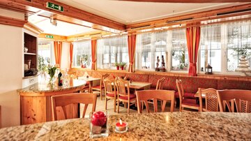 A cozy restaurant with wooden interior and plenty of seating. Bright curtains and an inviting atmosphere create a pleasant ambiance.