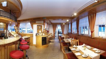 A cozy restaurant with wooden furniture and elegant decor. The tables are lovingly set and the atmosphere is inviting.