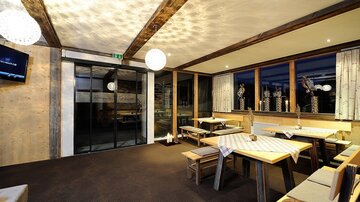 A modern restaurant with wooden ceilings and cozy seating. Large windows offer a view outside and provide plenty of light.