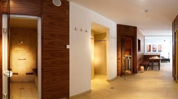 A modern wellness area with bright tiles and wooden paneling. There are showers, a sauna, and a relaxing lounge.