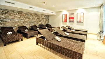 A relaxing wellness area with rattan loungers and a soothing stone wall. The soft lighting creates a calm atmosphere.