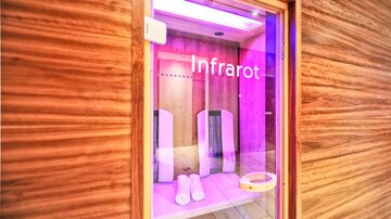 An infrared cabin with gentle lighting. The room has wooden walls and contains comfortable loungers.