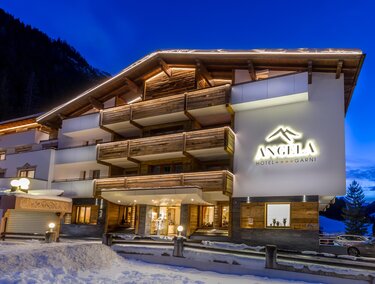 Ein modernes Hotelgebäude mit Holzverkleidung und beleuchteter Fassade in einer schneebedeckten Umgebung. Der Himmel ist in der Dämmerung, und die Atmosphäre ist einladend.