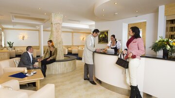 Eine elegante Lounge mit modernen Möbeln und einer Empfangstheke. Gäste interagieren entspannt miteinander und mit dem Personal.