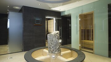 Ein moderner Wellnessbereich mit eleganten Glaswänden. In der Mitte steht ein runder Steinelement neben einer Sauna.
