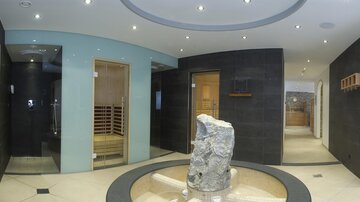 Ein eleganter Wellnessbereich mit modernen Einrichtungen und sanften Beleuchtungen. In der Mitte steht ein natürlicher Steinsockel, der dem Raum eine entspannende Atmosphäre verleiht.