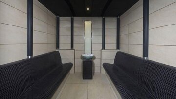 Ein moderner Wartebereich mit zwei langen Bänken und einem kleinen Tisch in der Mitte. Die Wände sind hell und minimalistisch gestaltet.