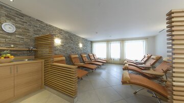 Ein entspannender Wellnessbereich mit Liegen und warmem Licht. Die Wände sind mit Naturstein verkleidet und es gibt eine moderne Holzverkleidung.