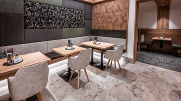 Ein modernes Restaurant mit eleganten Tischen und bequemen Stühlen. Die Wände sind mit verschiedenen Texturen und Holzpaneelen dekoriert.