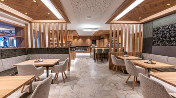 Ein modernes Restaurant mit Holz- und Steinelementen. Helle Tische und gemütliche Stühle schaffen eine einladende Atmosphäre.