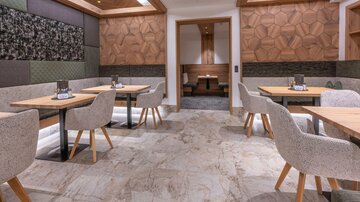 Ein modernes Restaurant mit stilvollen Tischen und gepolsterten Stühlen. Die Wände sind mit Holz und farbigen Paneelen dekoriert, während der Boden aus verschiedenen Steinarten besteht.