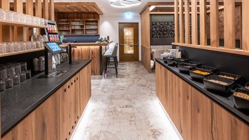 Eine moderne Esseria mit Holz- und Steinakzenten. Der Raum ist hell und einladend, mit einer Theke, die verschiedene Lebensmittel anbietet.