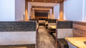Ein modernes Restaurant mit gemütlichen Sitzecken aus Holz und neutralen Farben. Die warme Beleuchtung schafft eine einladende Atmosphäre.