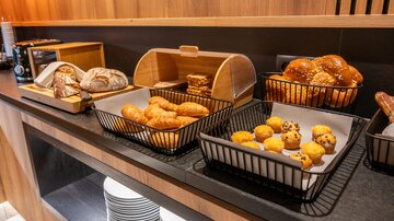 Ein Buffet mit verschiedenen Backwaren, darunter Brötchen, Croissants und kleine Muffins. Die Speisen sind in Körben auf einem dunklen Tisch angeordnet.