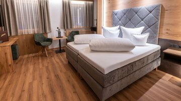 Ein modernes Schlafzimmer mit einem komfortablen Bett und eleganter Holzverkleidung. Die gemütliche Atmosphäre wird durch Tageslicht und stilvolle Möbel ergänzt.